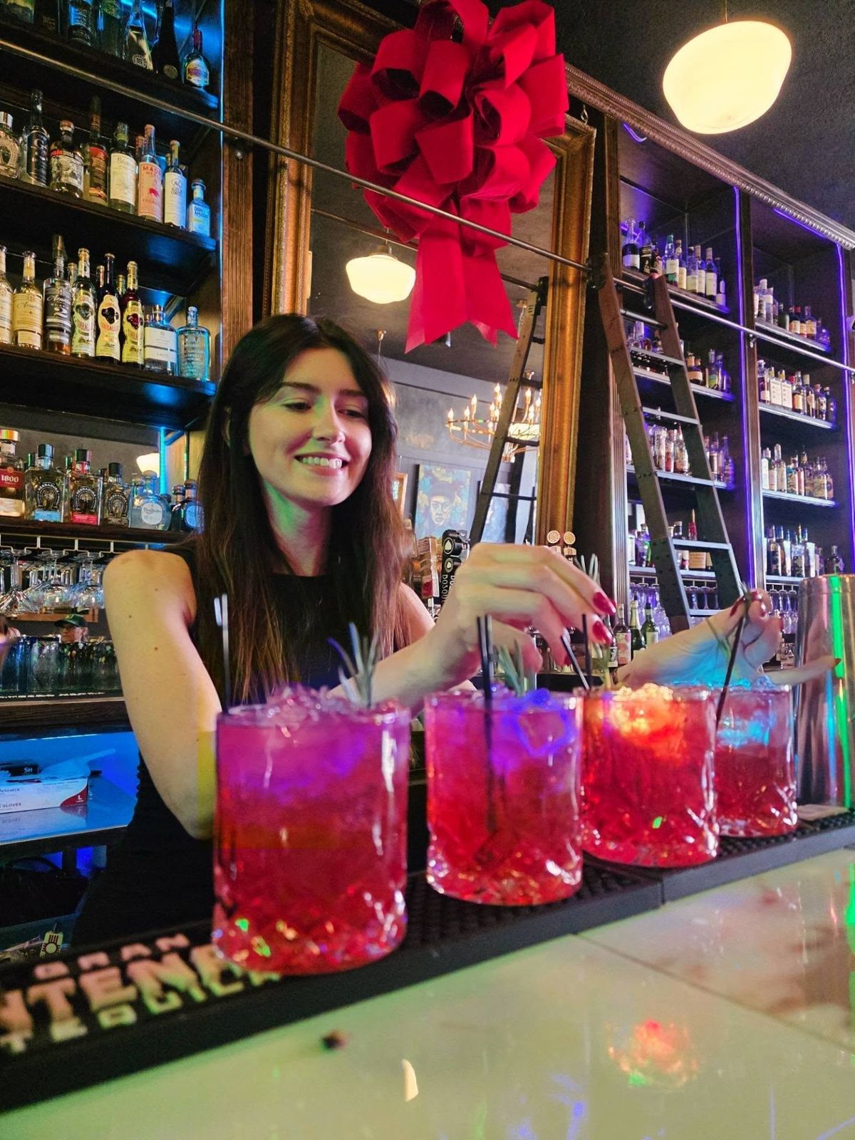 A Borracho's bartender garnishing a row of pink cocktails at the bar, under a big red holiday bow