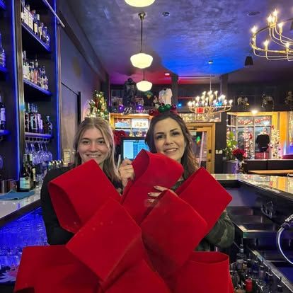 Two Borracho's team members smiling behind the bar, holding a giant red holiday bow
