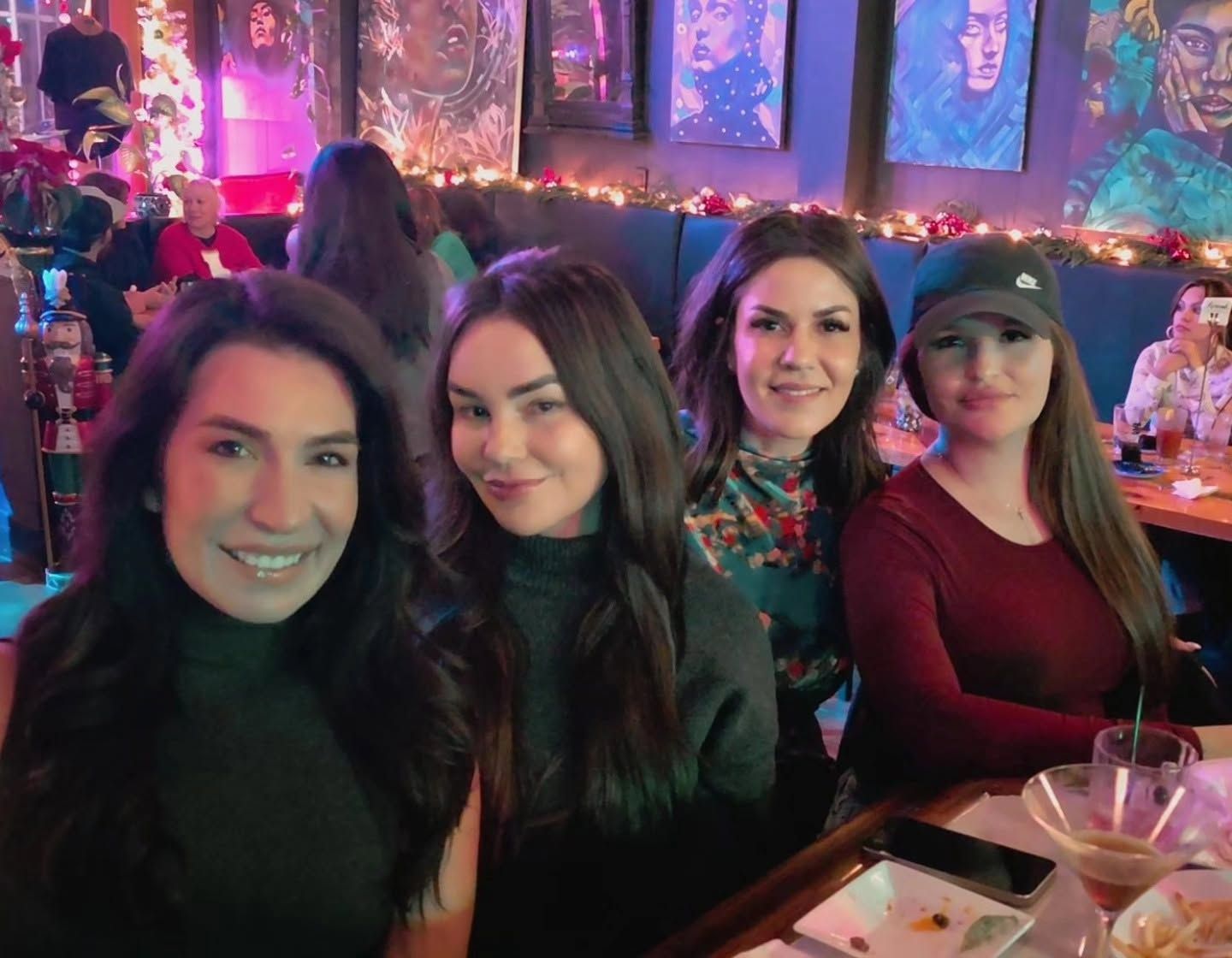 Four friends smiling at a table at Borracho's, with holiday garland and lights behind them